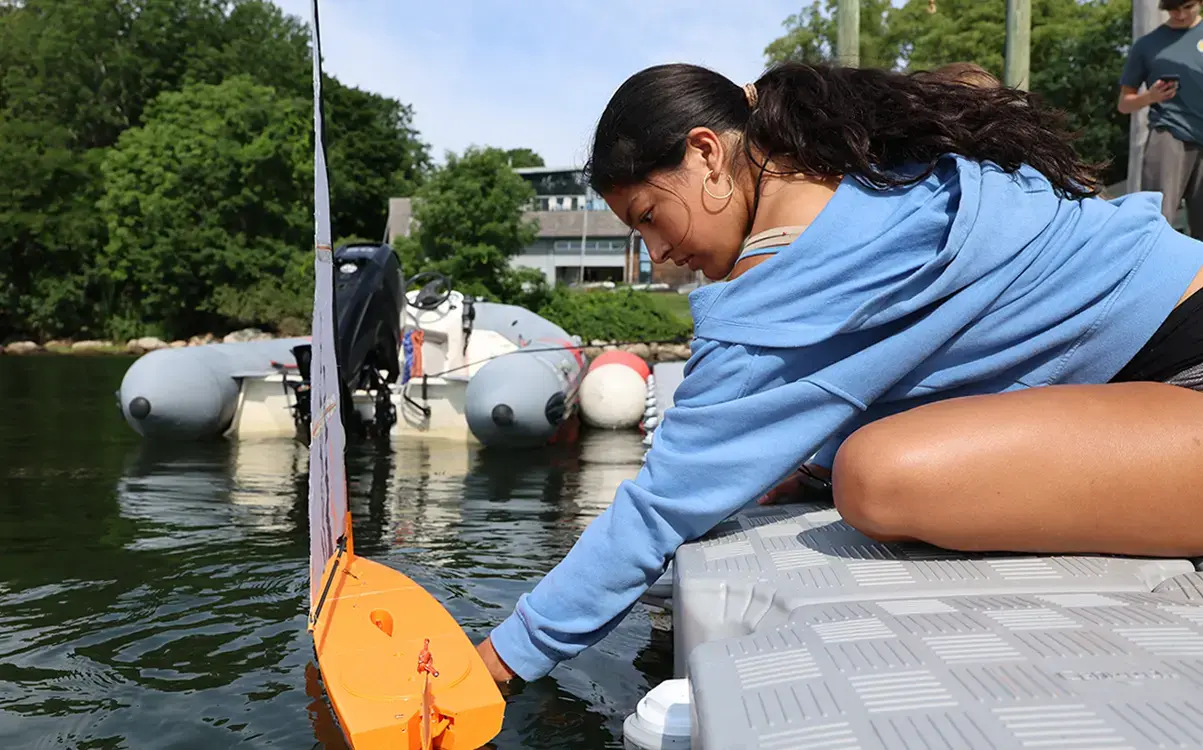Student launches model sailboat at the docks